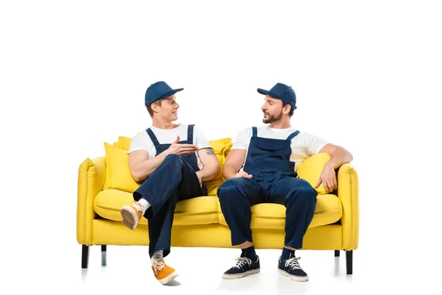 שני מובילים באוברול כחול יושבים על ספה צהובה ומתאמים ביניהם הובלת מכונת כביסה