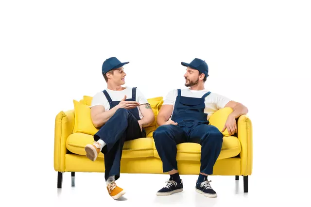 שני מובילים באוברול כחול יושבים על ספה צהובה ומתאמים ביניהם הובלת מכונת כביסה