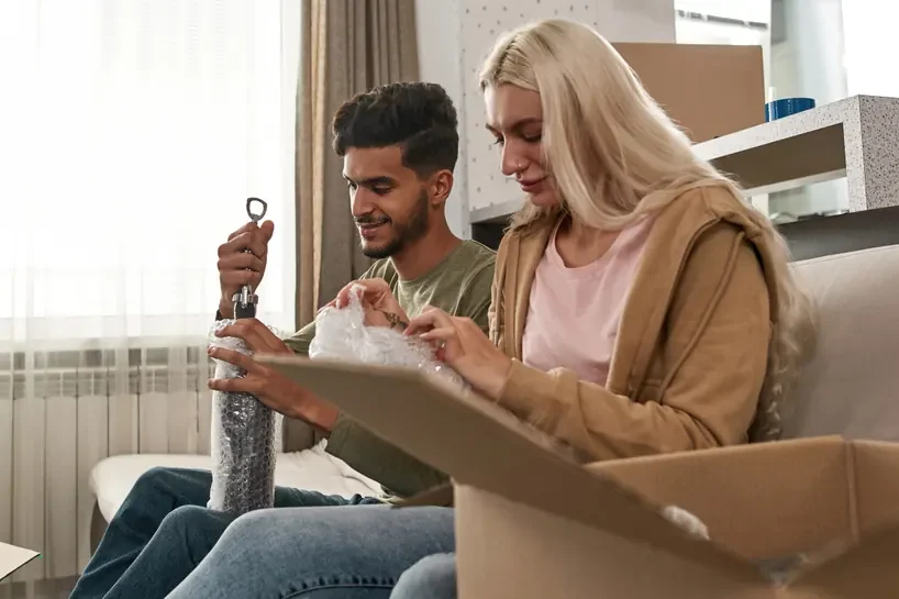 זוג עוטף בקבוק ביריעת בועות ליד ארגז קרטון פתוח בזמן אריזה למעבר