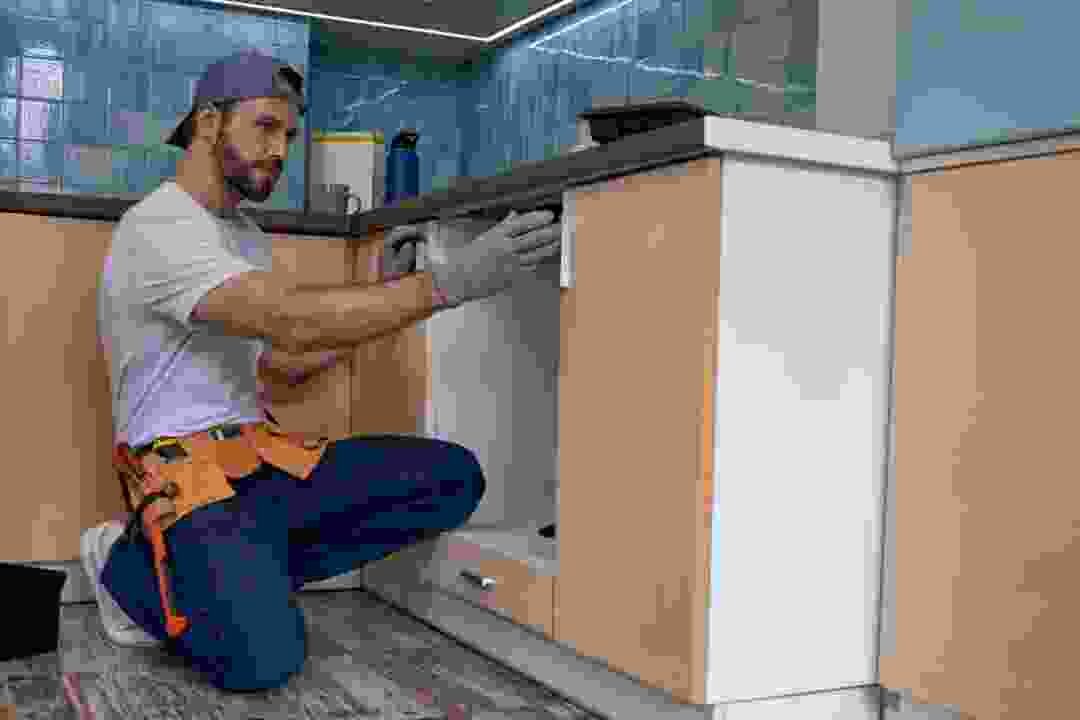 טכנאי כורע ליד ארונות מטבח ומכוון מכשיר לבן בתוך נישה מתחת לשיש