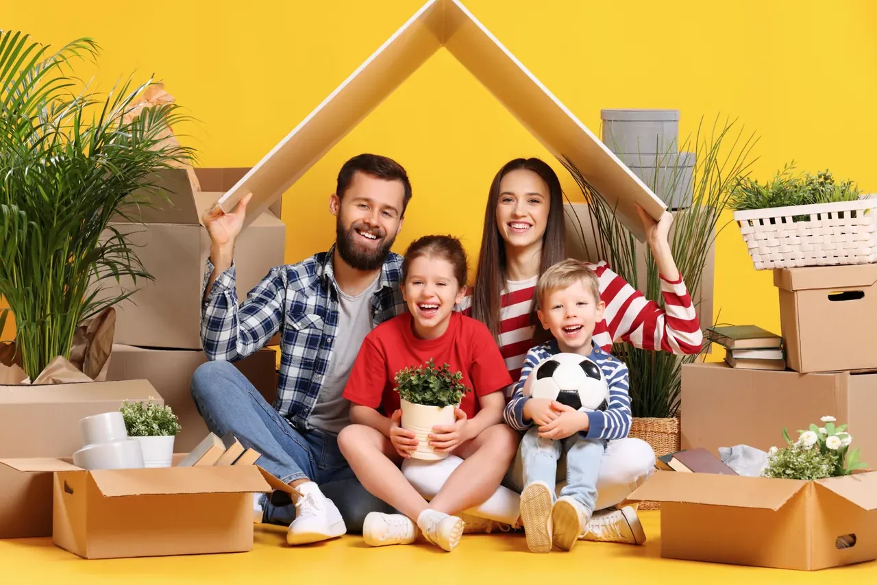 משפחה מחזיקה שני קרטונים בצורת גג מעל הראש על רקע צהוב