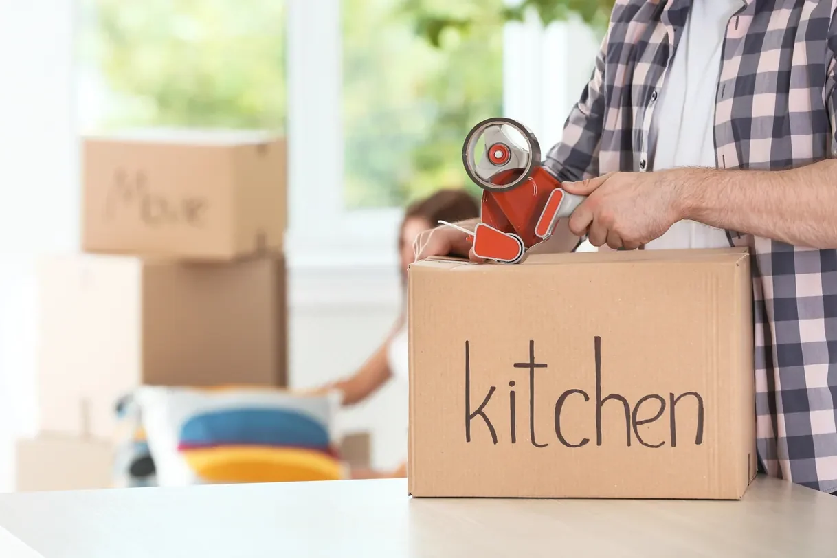 יד סוגרת בסרט הדבקה ארגז שעליו כתוב kitchen