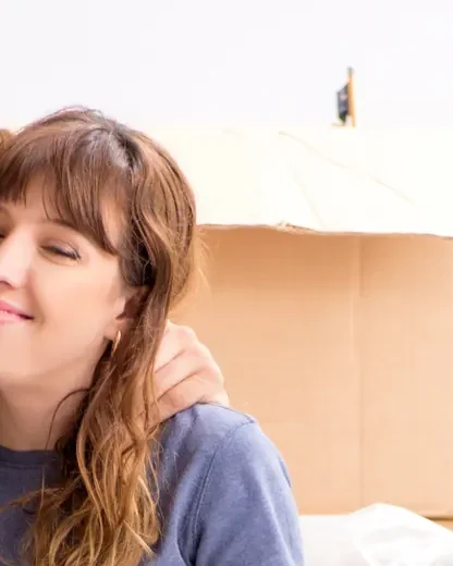 אישה מחייכת יושבת ליד ארגז קרטון גדול פתוח בחדר בהיר