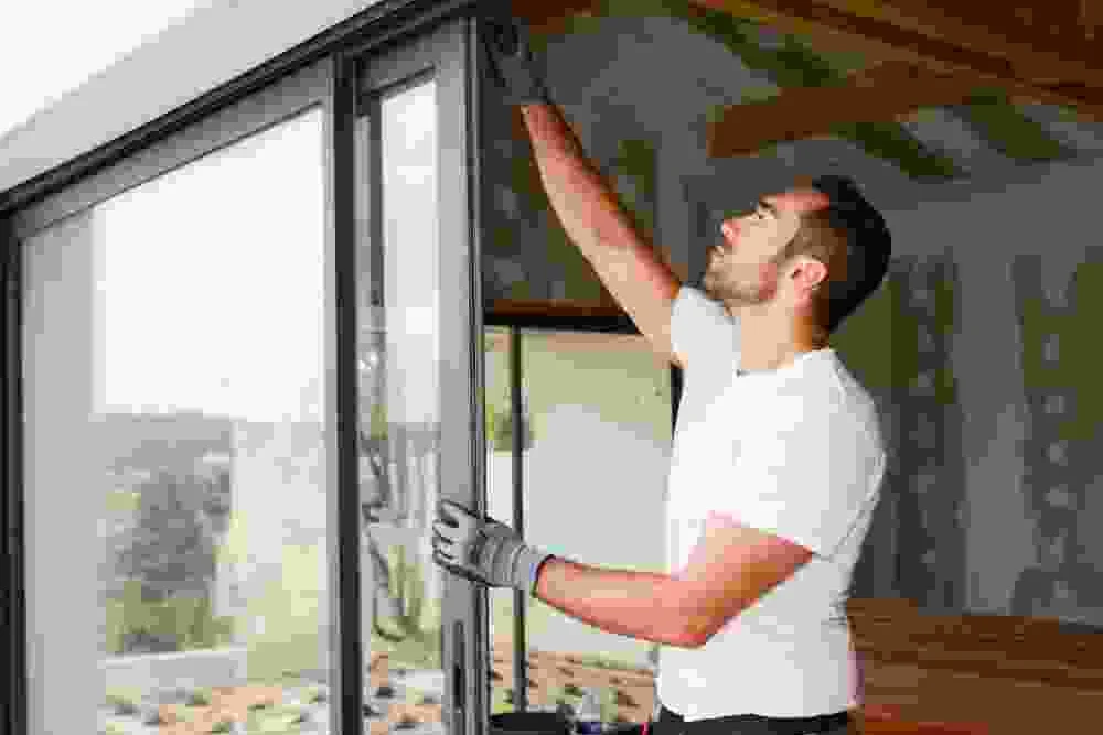עובד בחולצה לבנה בודק זגוגית גדולה בפתח יציאה למרפסת