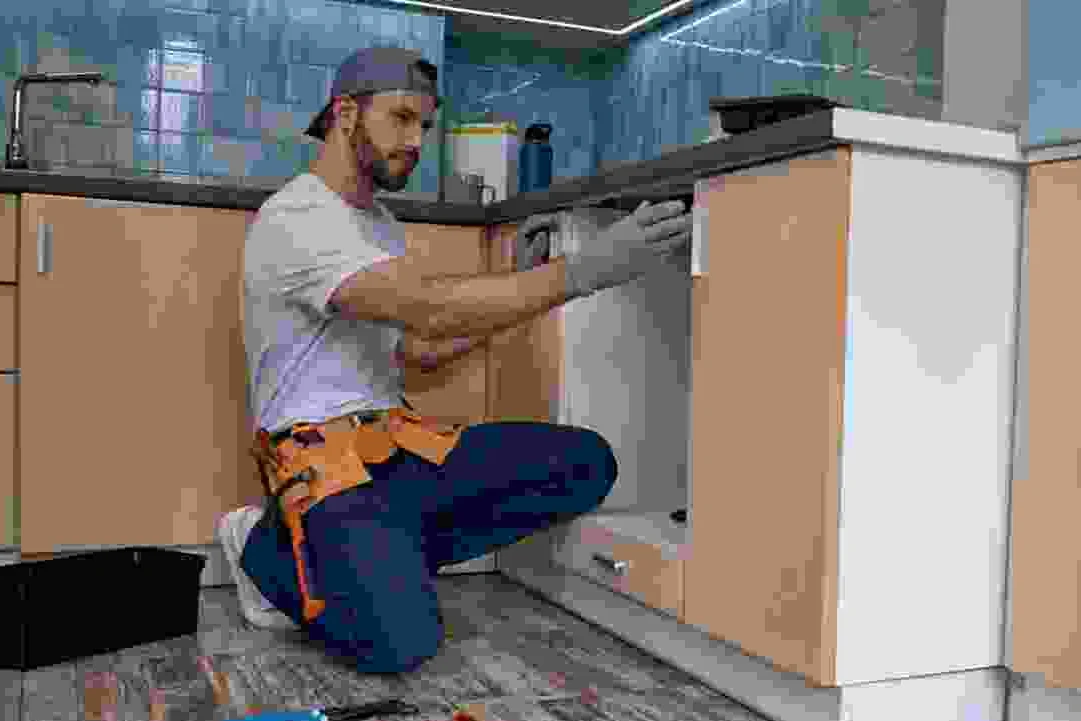 עובד יושב על הרצפה ומחבר צנרת מתחת לדלפק מטבח