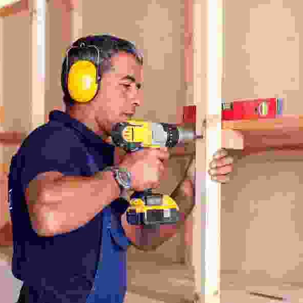 עובד עם מקדחה ופלס עומד מול פתח דלת בזמן התקנת משקוף