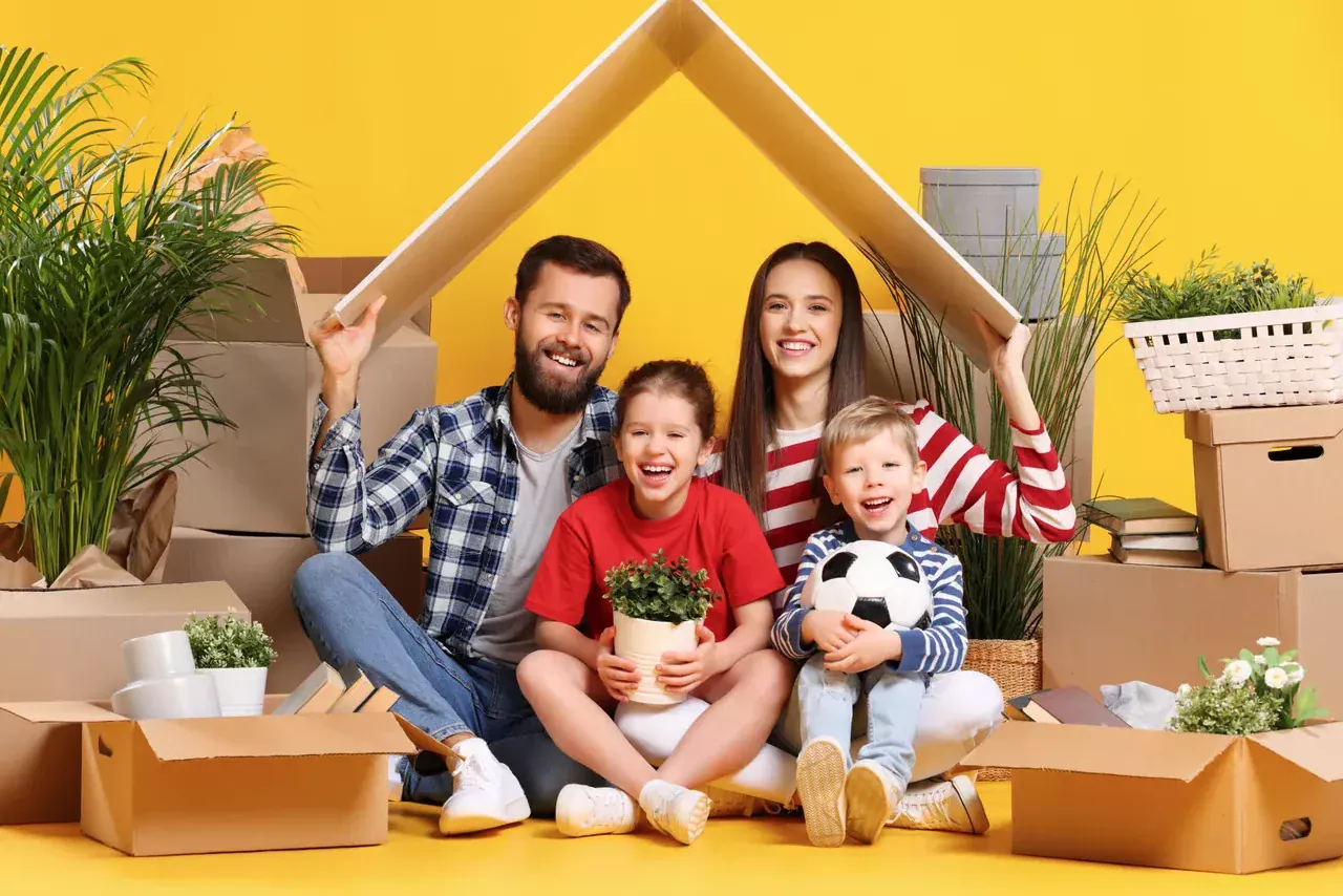 משפחה מחזיקה שני קרטונים בצורת גג מעל הראש על רקע צהוב
