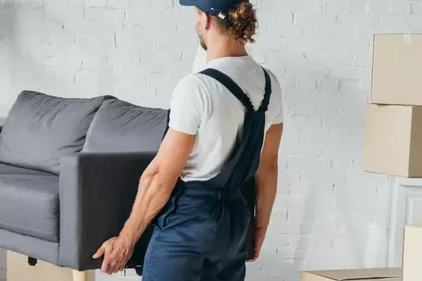 מוביל בסרבל עבודה נושא ספה אפורה ליד ארגזי קרטון